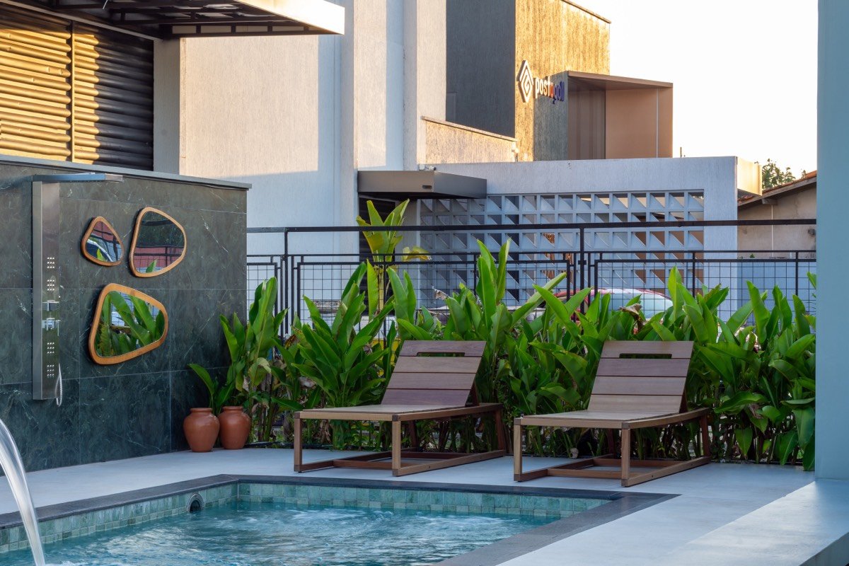 Área de lazer com piscina, espreguiçadeiras de madeira e jardim tropical